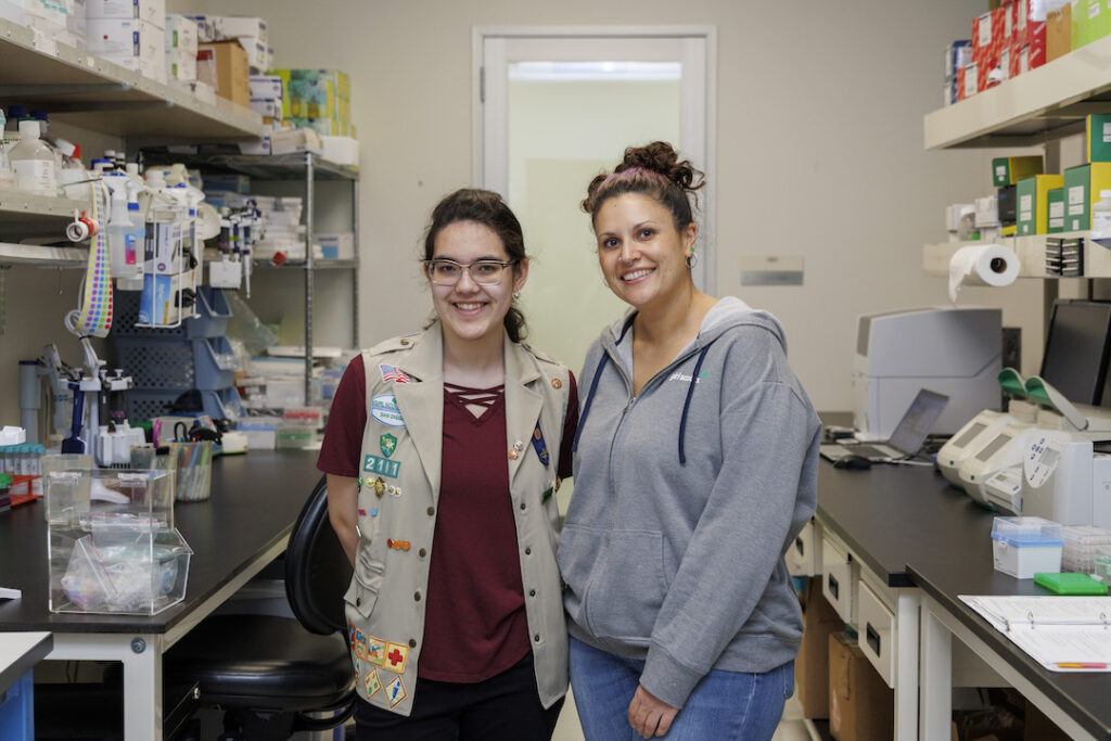 Ambassador Girl Scout Brielle A. stands to the left of LJI Next Generation Sequencing Core Director Suzie Alarcón in a lab setting. They are smiling at the camera.