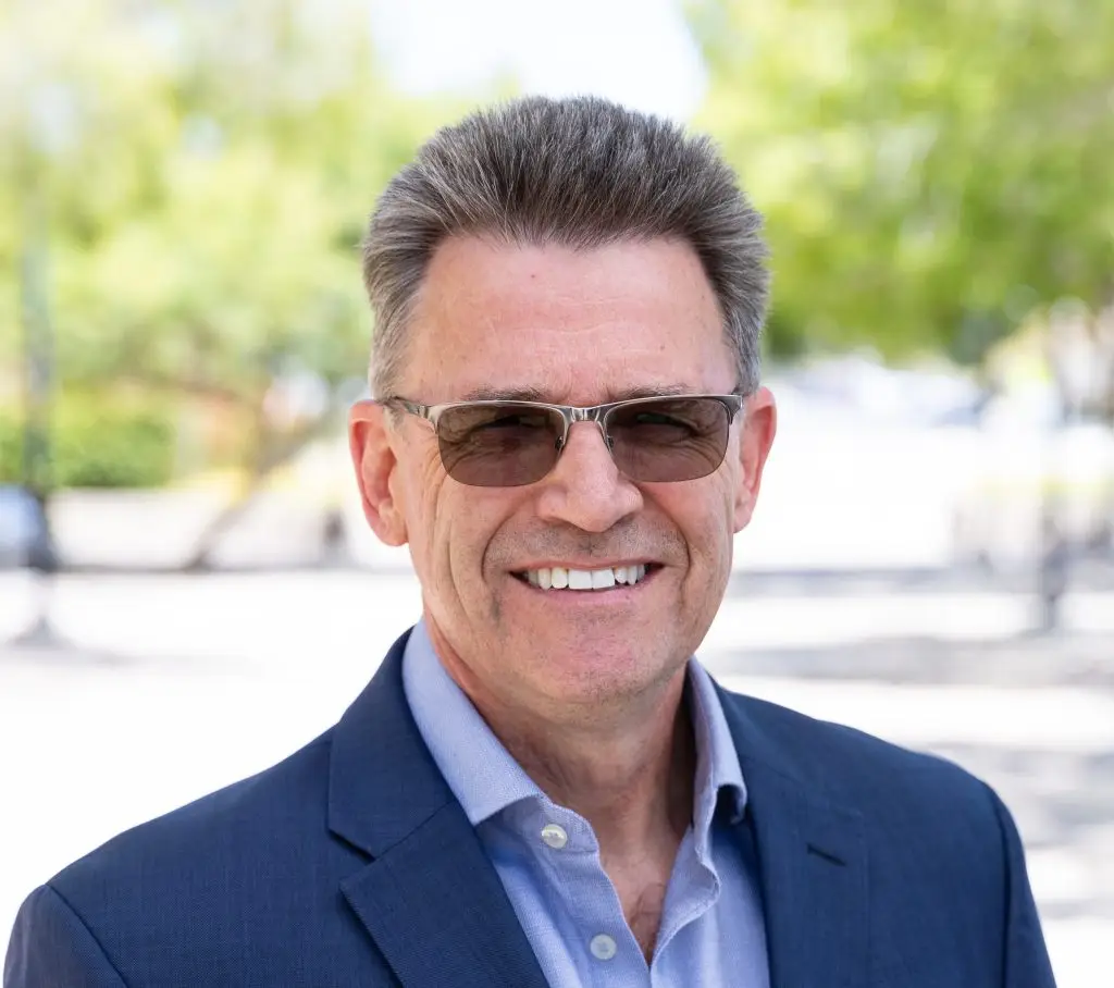 Portrait photo of Croft. He is wearing a suit and glasses. He is standing outside and smiling at the camera.